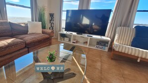 Un saló modern amb un sofà, una taula de centre de vidre, un televisor i vista a l'oceà.