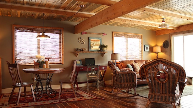 Una sala de estar acogedora con pisos de madera, una mesa de comedor con sillas, muebles de mimbre y un ventilador de techo.