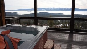 Een hottub op een houten terras met uitzicht op bergen en een meer.