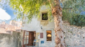 Un bâtiment rustique avec un mur en pierre, une porte en bois et une petite table entourée de chaises à l’extérieur.