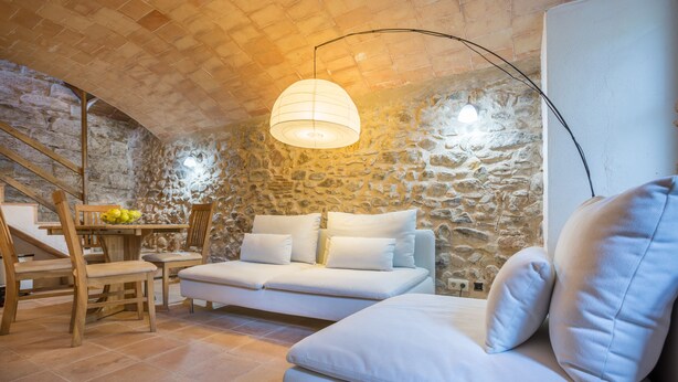 Un salon chaleureux avec un mur en pierre, un canapé blanc, une table à manger en bois avec des chaises et un escalier.