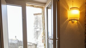 Une porte ouverte donnant sur un balcon d’où l’on peut admirer un mur de pierre et un arbre.