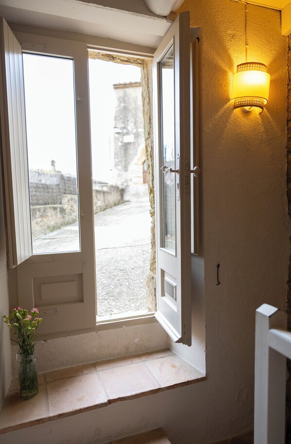 An open door leading to a balcony with a view of a stone wall and a tree.