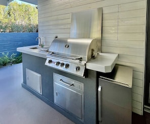 Eine Outdoor-Küche aus Edelstahl mit Grill, Spüle und Stauschubladen.