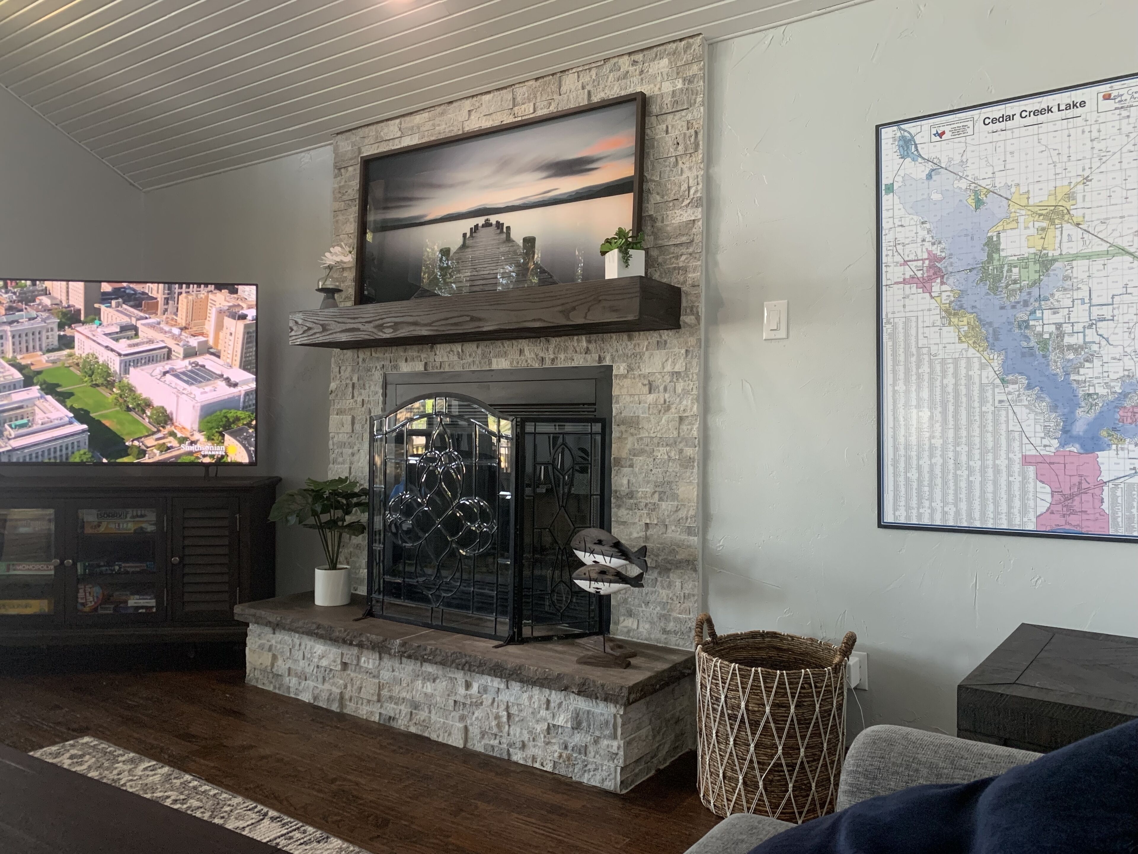 A living room with a stone fireplace, a mounted television displaying a cityscape, and a map on the wall.