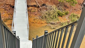 A metal staircase leading to a bridge over a river with trees in the background. - Log Cabin with large deck and dock in best location on the Lake! (mccormick)