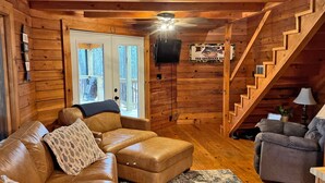 A log cabin interior with a leather sofa, a gray armchair, a wooden staircase, and a sign reading "The Savannah River". - Log Cabin with large deck and dock in best location on the Lake! (mccormick)