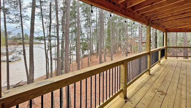 A wooden deck with a railing overlooking a forested area and a body of water. - Log Cabin with large deck and dock in best location on the Lake! (mccormick)