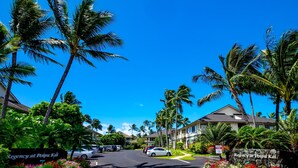 Straatbeeld van Regency at Poipu Kai, met een heldere lucht, palmbomen en een zebrapad dat naar de ingang van het hotel leidt.