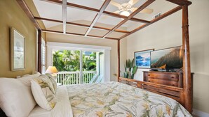 Een slaapkamer met een bed, een televisie, een houten dressoir en een balkon met uitzicht op groen.
