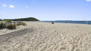 Une plage de sable parsemée d’empreintes, une clôture en bois et une colline qui se dessine à l’horizon.