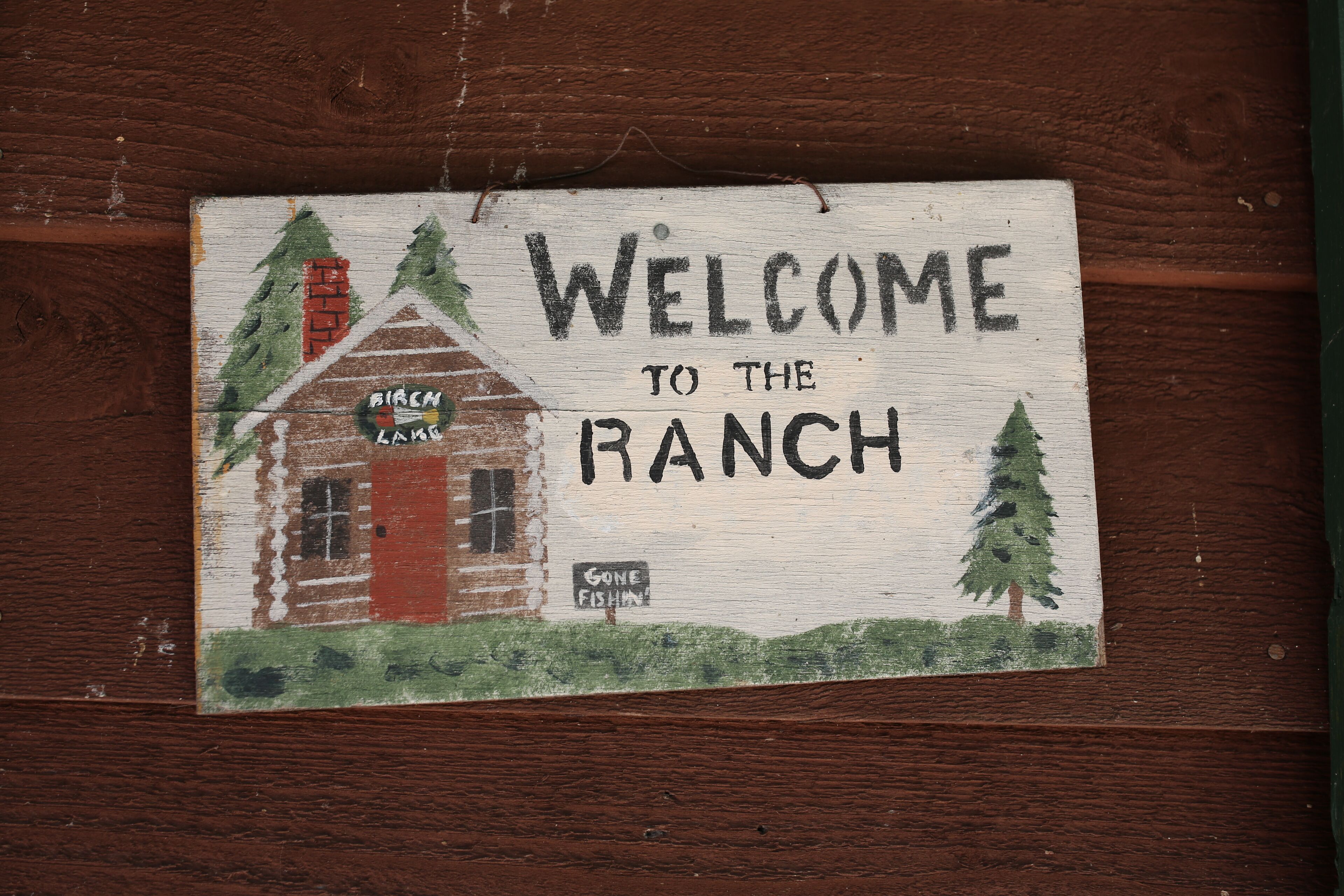 A welcome sign to the ranch with a rustic cabin illustration.