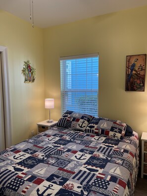 Relax in a cozy bedroom with a large bed, nautical-themed quilt, and a wall-mounted lamp.