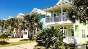 Une rangée de maisons colorées donnant sur la plage, dotées de balcons et entourées de palmiers.