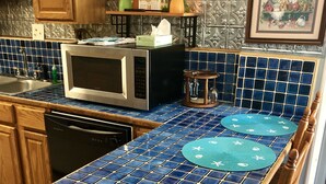 Uma cozinha com uma ilha revestida em azulejos azuis, armários de madeira, micro-ondas e pia.