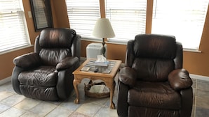 Quarto com duas poltronas de couro, uma pequena mesa de madeira com abajur e um cesto no chão.