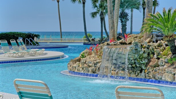 A pool with lounge chairs, a waterfall feature, and palm trees. - LONG BEACH RESORT Tower 2, 13th Floor 1 Bdr!!  Awesome Views! Beautiful Unit!!! ! (Panama City Beach)