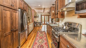 A kitchen with wooden cabinets, stainless steel appliances, and a patterned rug. - Gorgeous Rustic Ranch House & Farm Stay on 955 acre Ranch & Berry Farm-Sleeps 15 (Gaviota)