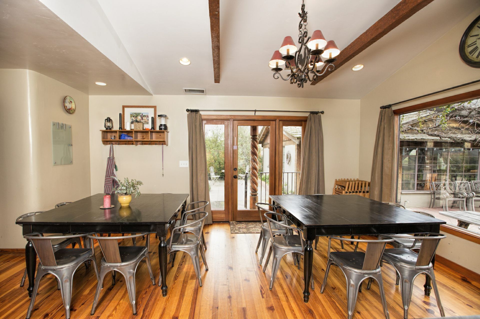 A dining area with a black table and metal chairs, wooden flooring, a chandelier, and a view through a glass door.