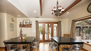 A dining area with a black table and metal chairs, wooden flooring, a chandelier, and a view through a glass door. - Gorgeous Rustic Ranch House & Farm Stay on 955 acre Ranch & Berry Farm-Sleeps 15 (Gaviota)