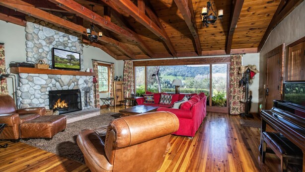 A spacious living room with a stone fireplace, leather furniture, and a large window offering a scenic view. - Gorgeous Rustic Ranch House & Farm Stay on 955 acre Ranch & Berry Farm-Sleeps 15 (Gaviota)