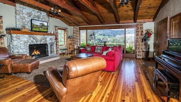 A spacious living room with a stone fireplace, leather furniture, and a large window offering a scenic view.