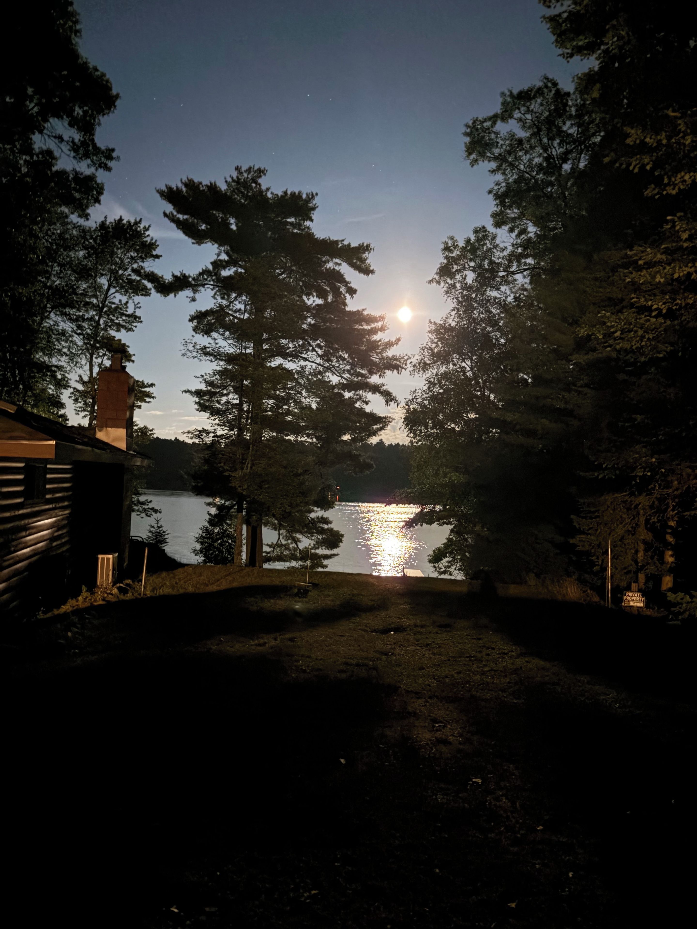 A nighttime view of a lake with a cabin and trees in the foreground.