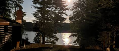 A nighttime view of a lake with a cabin and trees in the foreground.