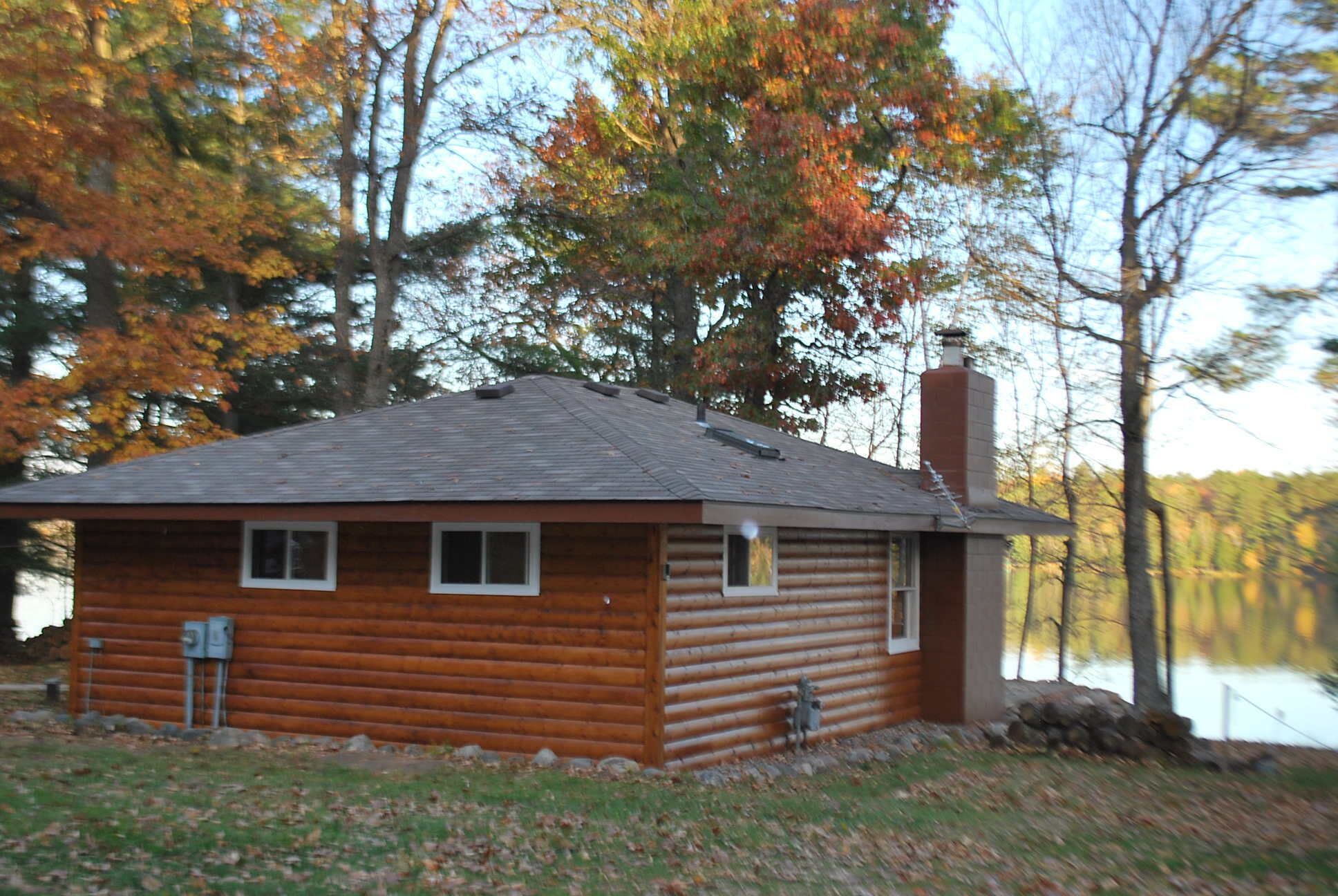 A log cabin with a sloped roof, a chimney, and a small porch with a statue.