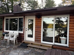 Eine Hütte mit einer Steinterrasse, zwei weißen Stühlen, einem Grill und Seeblick.