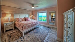 Une chambre à coucher avec un grand lit, une table de chevet, une commode et une vue sur l’extérieur par une fenêtre.