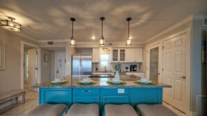 Une cuisine dotée d’un îlot central, de tabourets de bar, de luminaires suspendus et de meubles de rangement blancs.