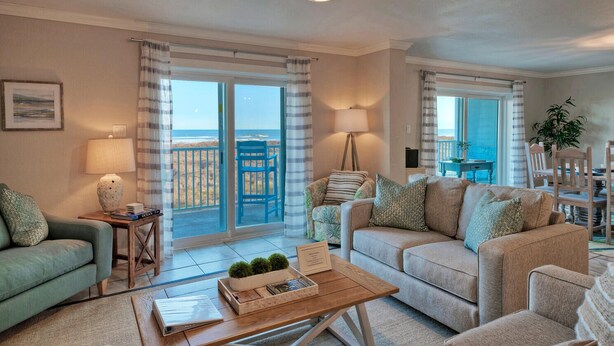 Un salon spacieux avec un grand canapé, une table basse et une vue sur la plage grâce aux portes-fenêtres coulissantes.