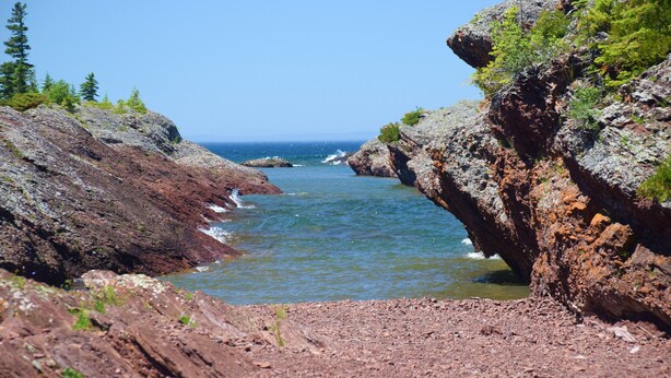 Paesaggio costiero roccioso con cielo azzurro intenso e onde oceaniche.