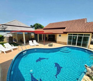 Una piscina con detalles de delfines, sillas de descanso y un área de patio cubierta.