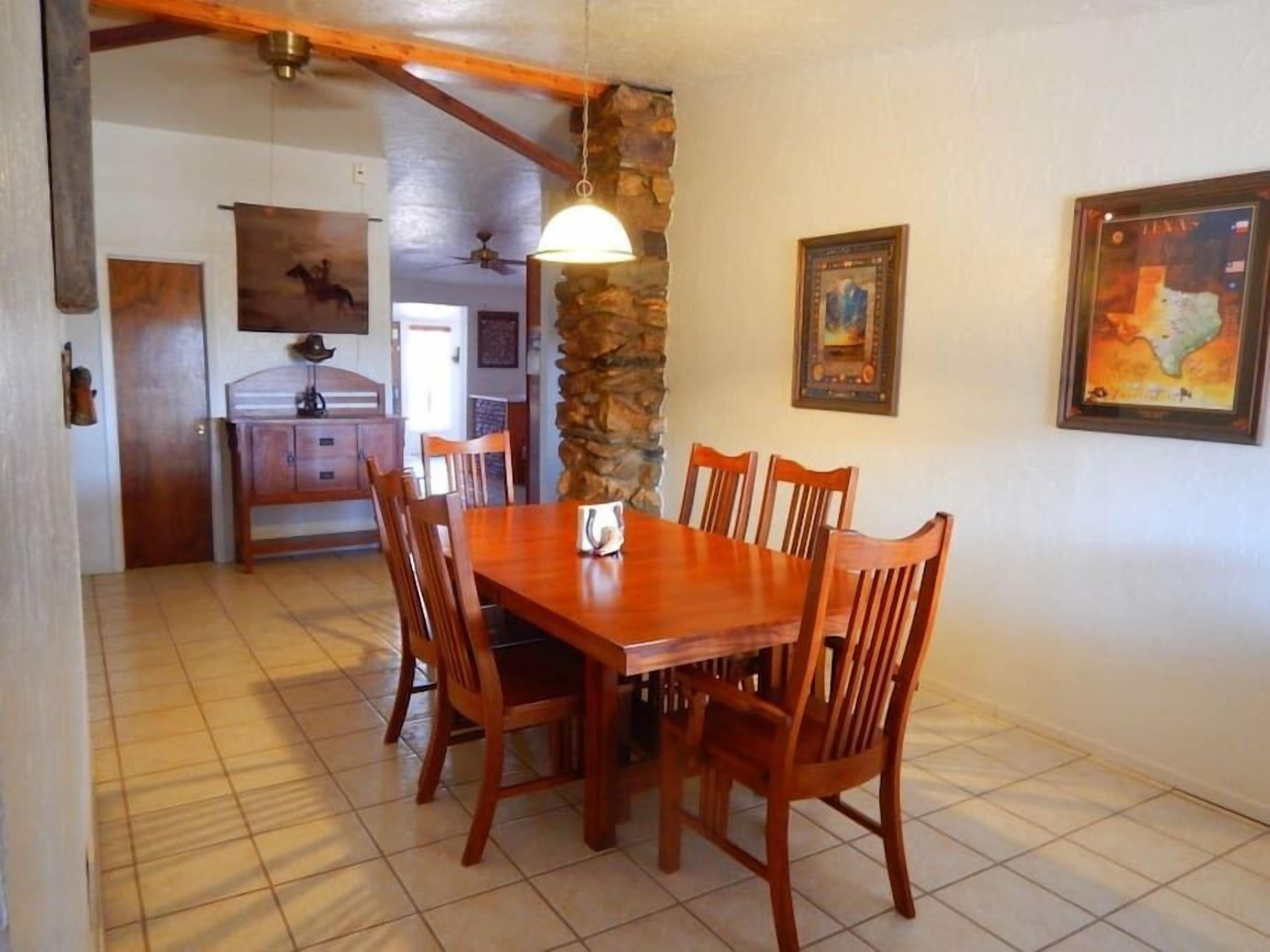 A dining area with a wooden table and chairs, a stone wall, and framed artwork on the walls.