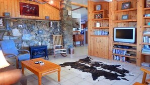 A rustic living room with a stone wall, wooden shelves, a television, and a cowhide rug.