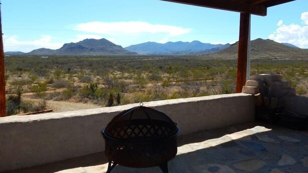 A covered outdoor area with a metal grill, a stone floor, and a view of a desert landscape with mountains in the distance.