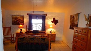 A bedroom with a bed, two bedside tables with lamps, a wooden dresser, a chair, and a cowhide rug.