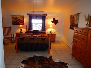 Une chambre à coucher comprenant un lit, deux tables de chevet avec des lampes, une commode en bois, une chaise et un tapis en peau de vache.