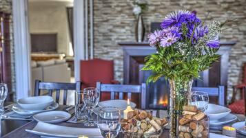Une table à manger est dressée avec des assiettes, des verres et une bougie. On y trouve un vase rempli de fleurs et un bol de bouchons de liège.