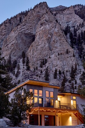 Un bâtiment moderne à deux étages, doté d’un balcon, de grandes fenêtres et offrant une vue sur une montagne rocheuse.