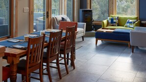 Ein geräumiges Zimmer mit großen Fenstern, einem Essbereich mit Holzsesseln, einer Couch und einem Deckenventilator.