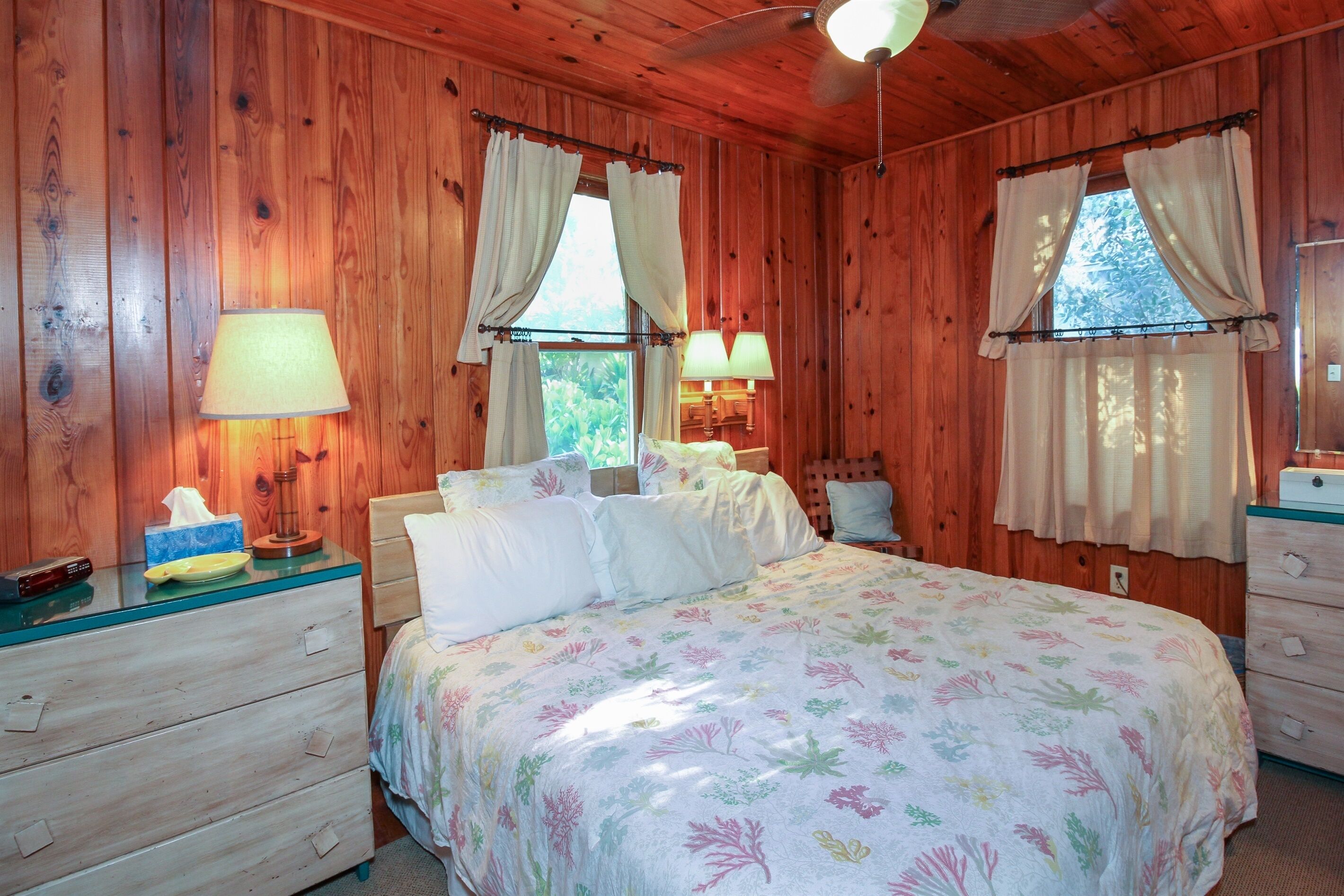 A wooden cabin bedroom with a bed, two bedside lamps, a nightstand, and a dresser.