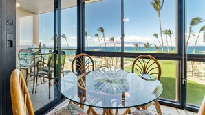 Comedor con paredes de vidrio que ofrece vistas a una playa con palmeras y un cielo despejado.