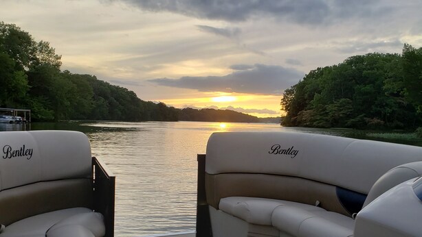Un bote con la marca 'Bentley' y una vista de un lago con árboles y un cielo nublado.