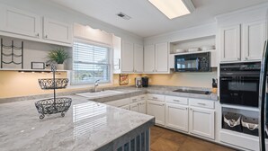 Una cocina moderna con armarios blancos, encimera de mármol, microondas integrado y refrigerador.
