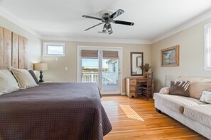 Een slaapkamer met een bed, een dressoir, een bureau, een plafondventilator en een balkon.