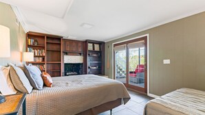 Un dormitorio con una cama grande, una estantería, una chimenea y un ventanal corredera a un balcón.