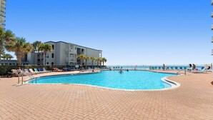 A swimming pool with lounge chairs and palm trees, surrounded by a building with balconies. - Tidewater Beach Resort 2009 Last minute Discounts. Bunk bed room (Panama City Beach)